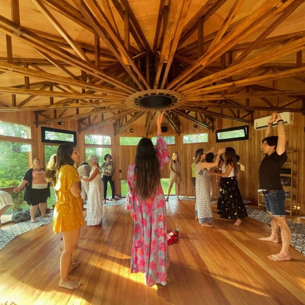 Grupo de personas en círculo vivencial guiado por Cata Heincke, en un espacio de madera sagrado, reconectando con su esencia.