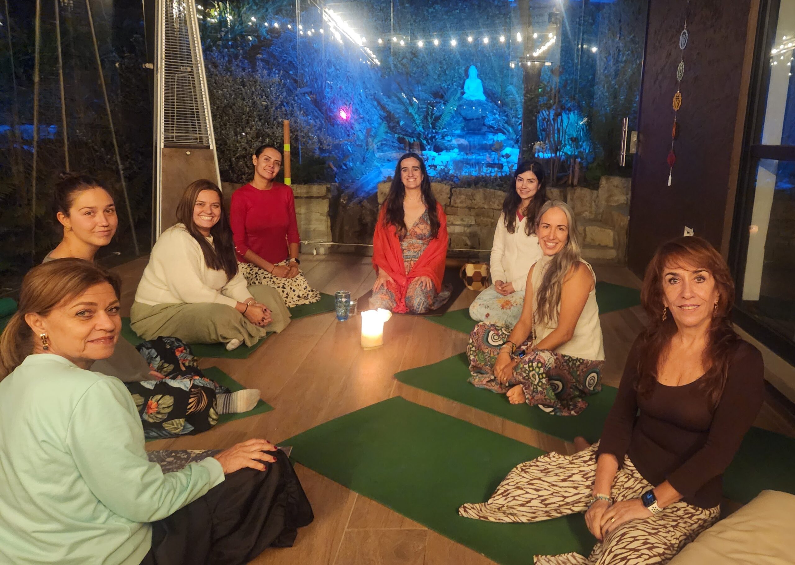 Grupo de mujeres acompañadas por Cata Heincke en un círculo íntimo con velas, simbolizando la integración de modalidades presenciales, virtuales y personalizadas.