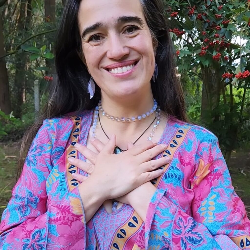 Cata Heincke sonriendo con las manos sobre el corazón, en un entorno natural, reflejando autenticidad y gratitud en su camino espiritual.