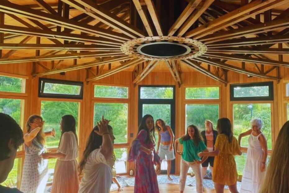 Mujeres y hombres en círculo sagrado danzando descalzos en un espacio de madera, durante una sesión presencial de la Danza del Fénix guiada por Cata Heincke.